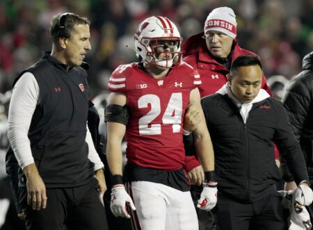 Wisconsin head coach Luke Fickell, left, helps safety Hunter Wohler (24) get off the field