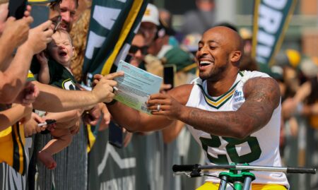 Green Bay Packers running back A.J. Dillon signs a copy of his childrenÕs book for a fan as he rides a bicycle to practice in the Dream Drive during the first day of training camp on Monday, July 22, 2024, at Lambeau Field in Green Bay, Wis. Tork Mason/USA TODAY NETWORK-Wisconsin